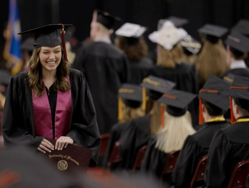 A graduate smiling and holding her diploma