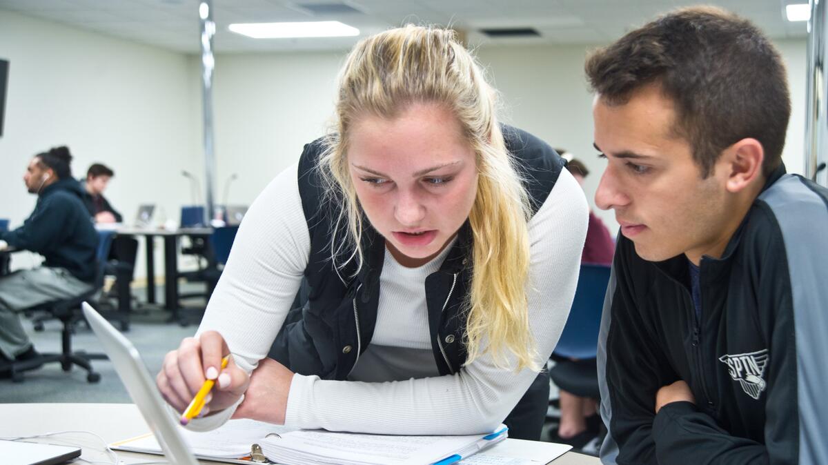 Two students study together with a laptop in the library. 